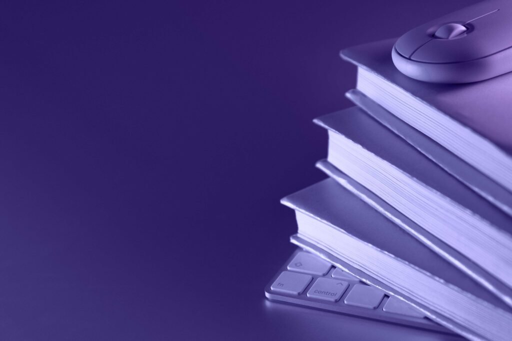 Pile de livres, clavier et souris d'ordinateur sur fond violet. Image représentant la page blog de la librairie en ligne Au Repaire de l'Imaginaire. texte : Au Repaire de l'Imaginaire Le Blog